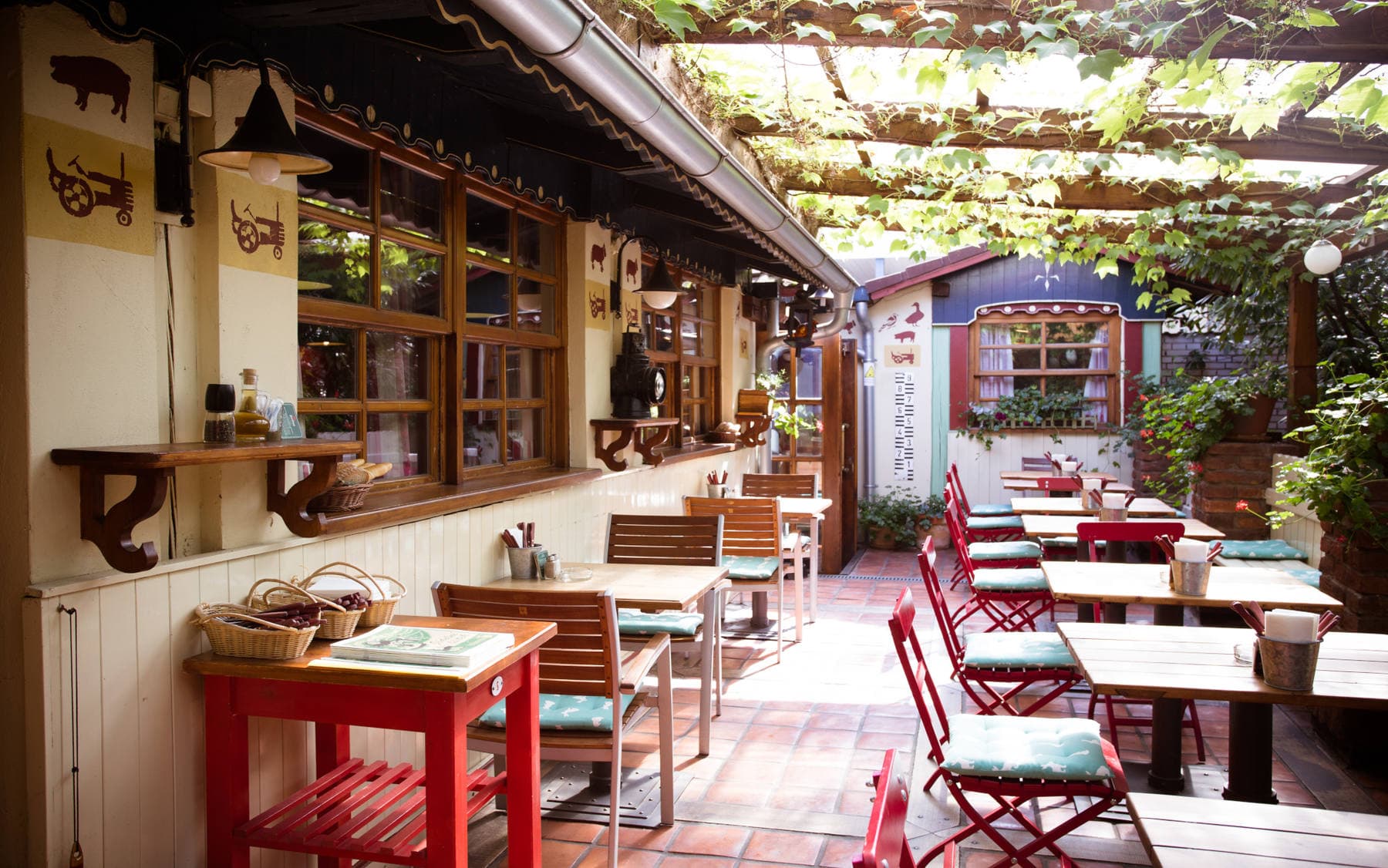 Letní zahrádka U Kašpárka pod pergolou z vinné révy s červenými bistro židlemi